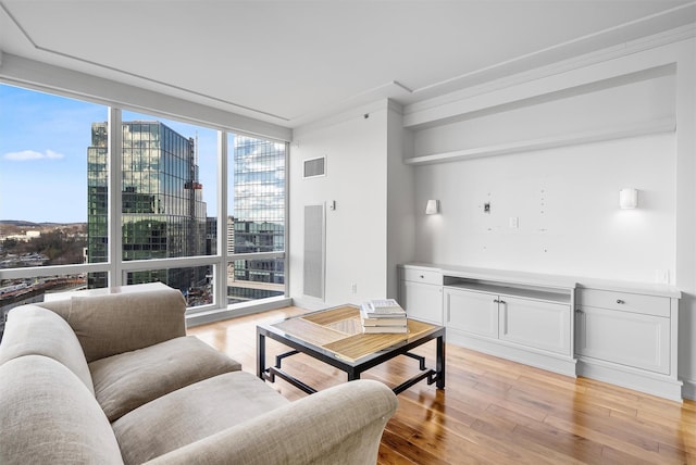 living room featuring expansive windows, light wood-style flooring, visible vents, and a city view