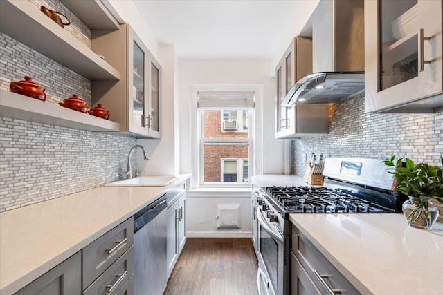 kitchen featuring stainless steel appliances, a sink, light countertops, wall chimney range hood, and open shelves