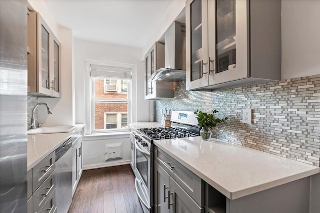 kitchen featuring gray cabinetry, a sink, wall chimney range hood, appliances with stainless steel finishes, and backsplash