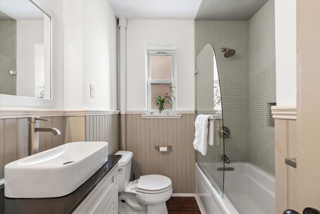 bathroom with bathtub / shower combination, toilet, wood finished floors, vanity, and wainscoting