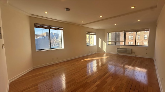 empty room featuring an AC wall unit, plenty of natural light, baseboards, and wood finished floors