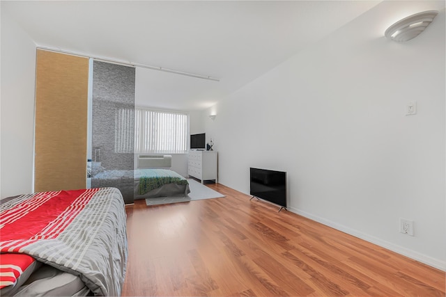 bedroom with a wall mounted air conditioner, wood finished floors, and baseboards