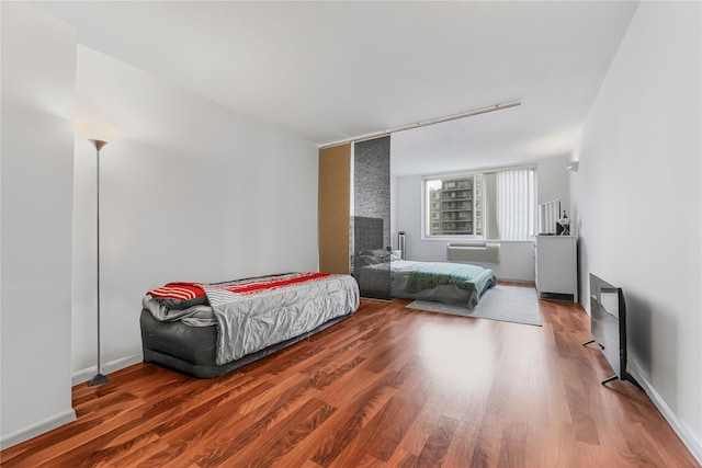 bedroom with a wall unit AC, wood finished floors, and baseboards