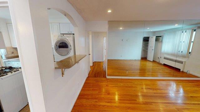 interior space featuring arched walkways, wood finished floors, white cabinets, radiator, and washer / dryer