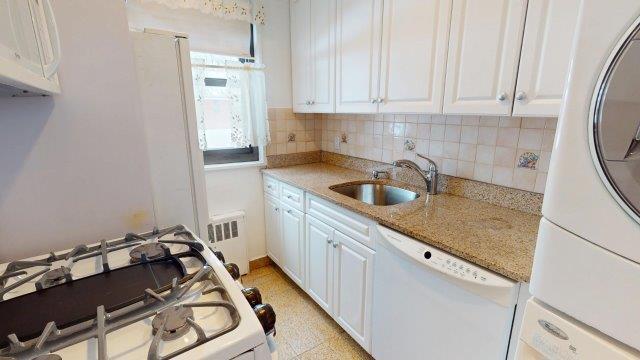 kitchen with white appliances, radiator heating unit, a sink, and white cabinets