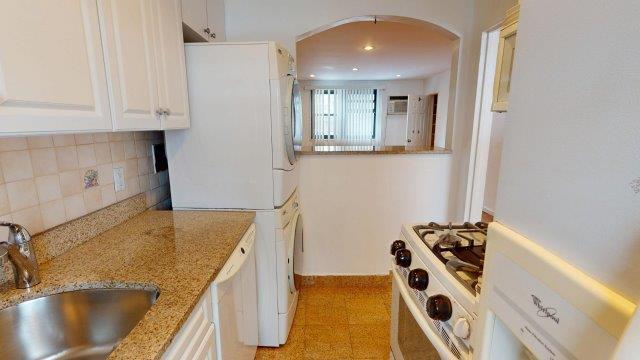 kitchen with arched walkways, light stone counters, a sink, white cabinets, and stacked washing maching and dryer