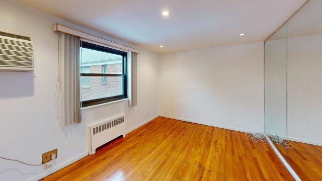 spare room with baseboards, radiator heating unit, light wood-style flooring, a wall mounted air conditioner, and recessed lighting