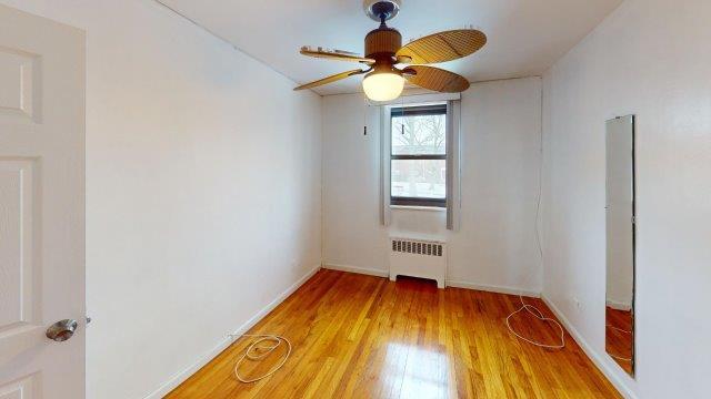 unfurnished room with baseboards, ceiling fan, light wood-style flooring, and radiator