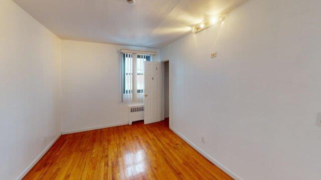 spare room with baseboards, radiator heating unit, and wood finished floors