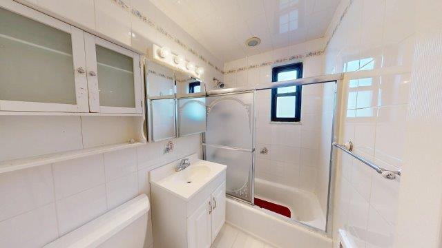 bathroom with toilet, bath / shower combo with glass door, vanity, tile walls, and decorative backsplash