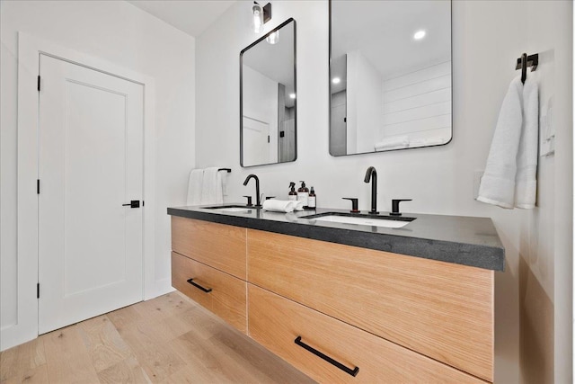 bathroom with double vanity, wood finished floors, a sink, and recessed lighting