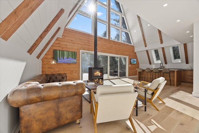 living area featuring beam ceiling, wood walls, light wood finished floors, and a wood stove