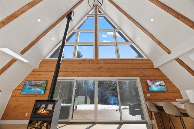 unfurnished living room with high vaulted ceiling, wood walls, beamed ceiling, and a wood stove