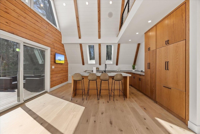 interior space with vaulted ceiling with beams, light wood-style floors, modern cabinets, and wooden walls