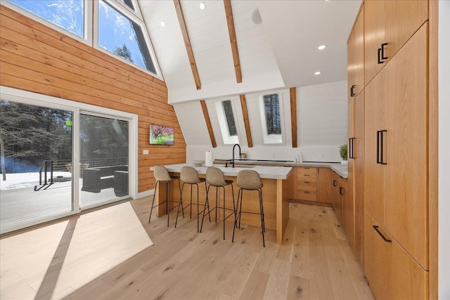 kitchen featuring a breakfast bar, a center island with sink, light countertops, wooden walls, and modern cabinets