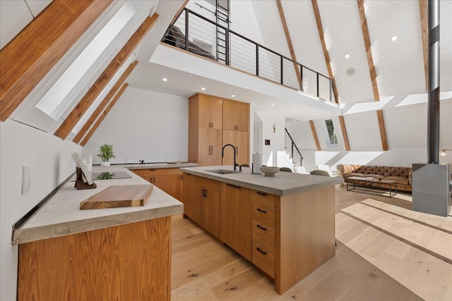 kitchen with light wood finished floors, a center island with sink, beam ceiling, and a sink