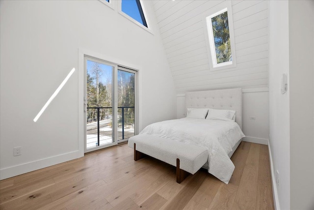 bedroom featuring access to outside, a high ceiling, light wood-type flooring, and baseboards