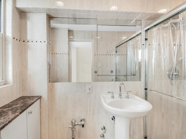 bathroom with a stall shower, a sink, and tile walls