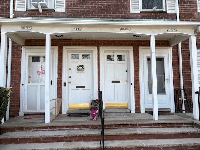 doorway to property with a porch and brick siding