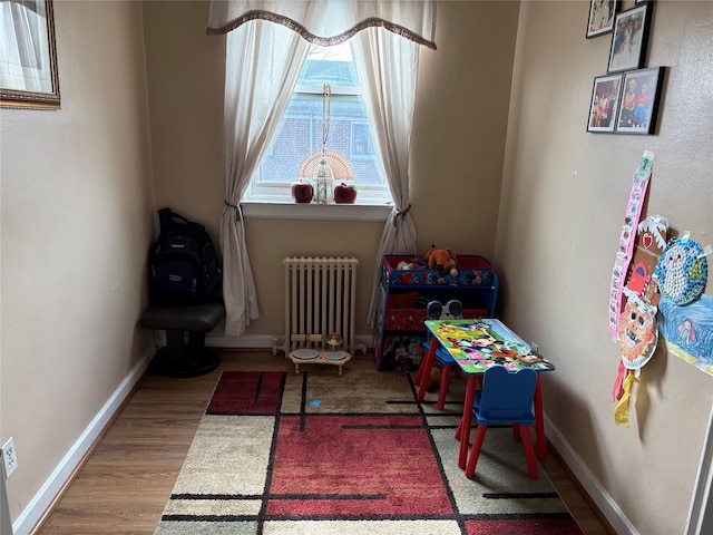 playroom featuring radiator heating unit, baseboards, and wood finished floors