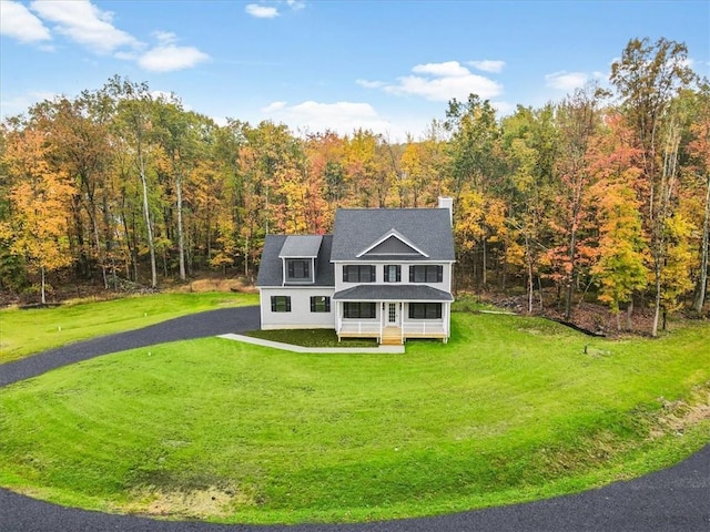 view of front of home featuring covered porch, a chimney, a front lawn, and a wooded view