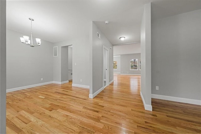 empty room featuring a chandelier, light wood-type flooring, visible vents, and baseboards