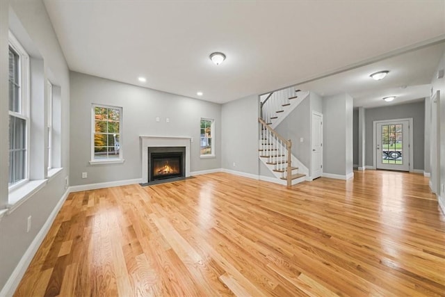 unfurnished living room featuring recessed lighting, a fireplace with flush hearth, baseboards, light wood-style floors, and stairway