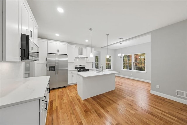 kitchen featuring stainless steel appliances, wall chimney range hood, an island with sink, and white cabinets