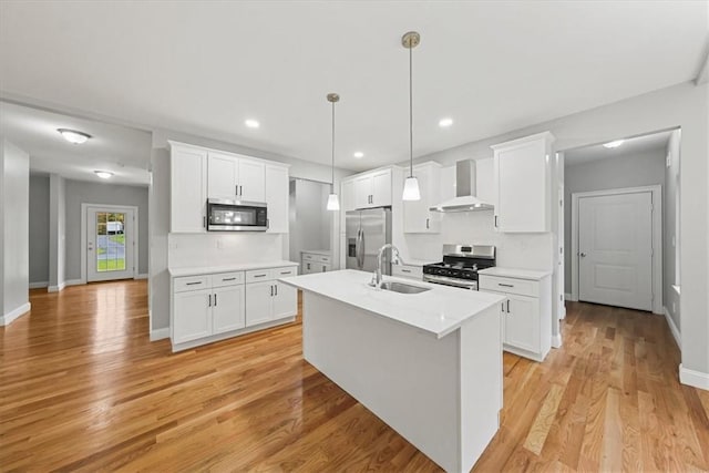 kitchen featuring appliances with stainless steel finishes, light countertops, wall chimney range hood, white cabinetry, and a sink