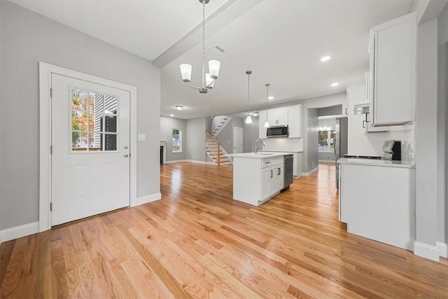 kitchen featuring a center island with sink, stainless steel appliances, light countertops, hanging light fixtures, and white cabinetry