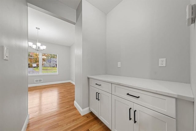 corridor featuring light wood finished floors, baseboards, visible vents, and a chandelier