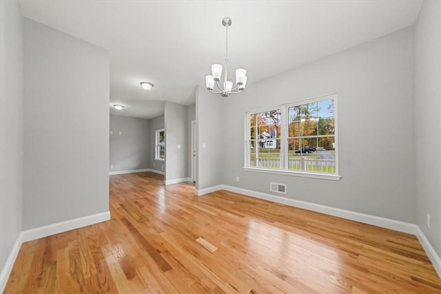 unfurnished dining area with baseboards, wood finished floors, visible vents, and an inviting chandelier