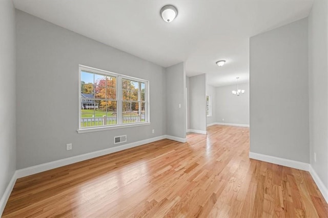 spare room with light wood finished floors, an inviting chandelier, visible vents, and baseboards