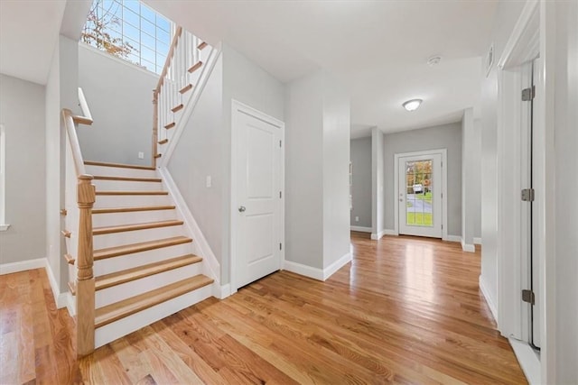 foyer with light wood-style floors, baseboards, and stairway