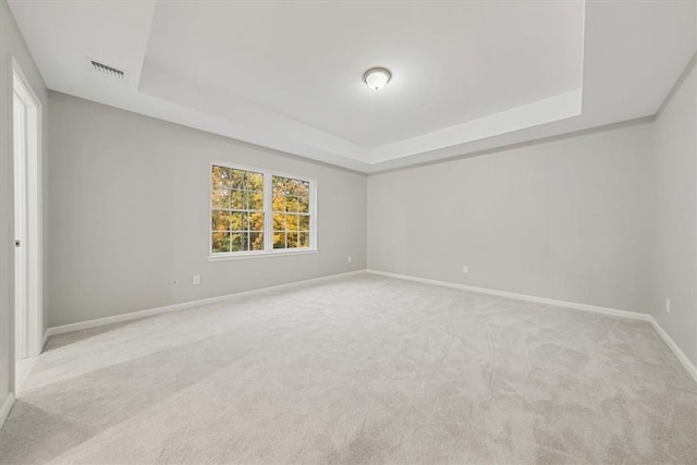 empty room with a tray ceiling, visible vents, and light carpet