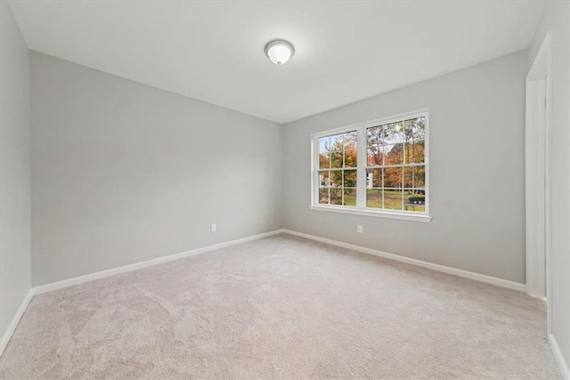 spare room featuring light colored carpet and baseboards