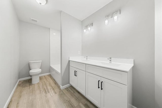 bathroom with double vanity, toilet, a sink, wood finished floors, and baseboards