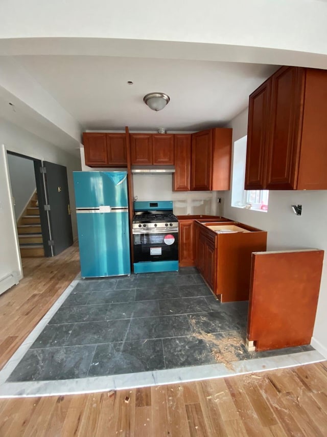 kitchen featuring stainless steel range with gas cooktop, dark wood-type flooring, freestanding refrigerator, brown cabinetry, and under cabinet range hood