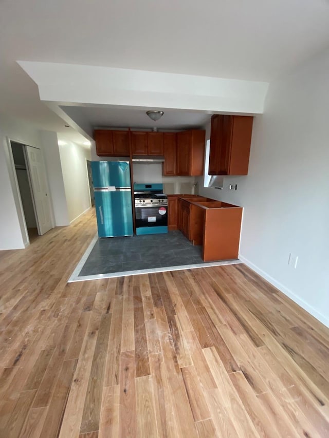 kitchen with light wood finished floors, baseboards, brown cabinetry, refrigerator, and stainless steel stove