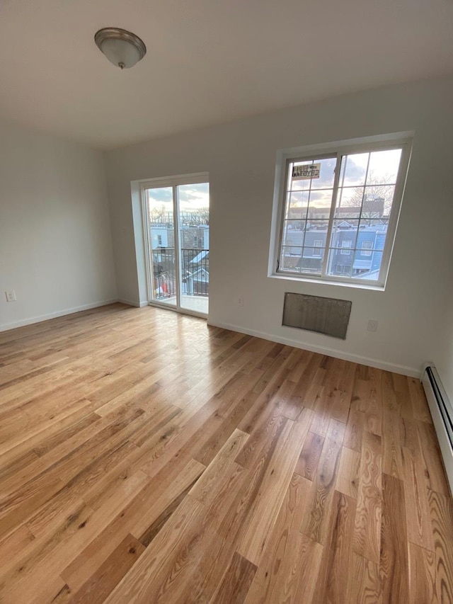 unfurnished room featuring a baseboard heating unit, light wood finished floors, and baseboards