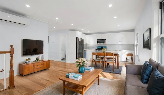 living area with attic access, recessed lighting, a wall mounted air conditioner, and light wood-style flooring