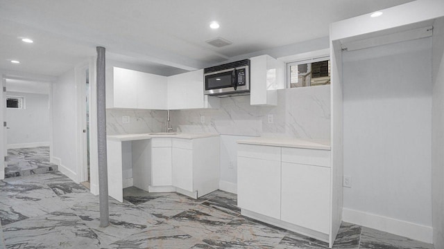 kitchen with tasteful backsplash, stainless steel microwave, marble finish floor, light countertops, and white cabinetry