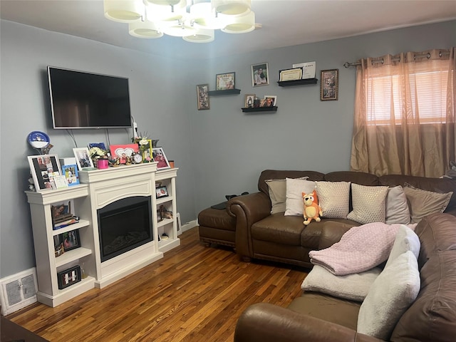 living area with a fireplace, visible vents, an inviting chandelier, wood finished floors, and baseboards