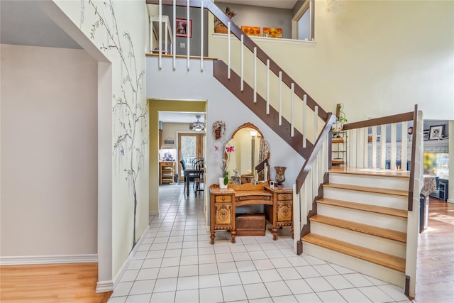 staircase with a ceiling fan, tile patterned flooring, baseboards, and a high ceiling