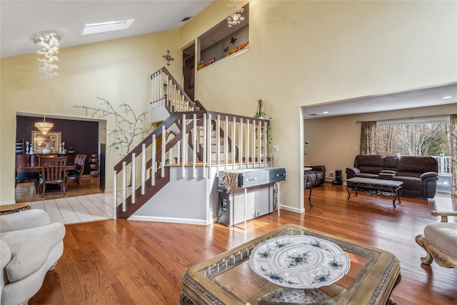 living room with a skylight, stairway, a towering ceiling, wood finished floors, and baseboards