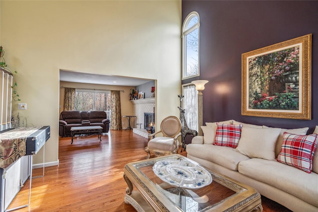 living room featuring light wood-type flooring, a high ceiling, a fireplace, and baseboards