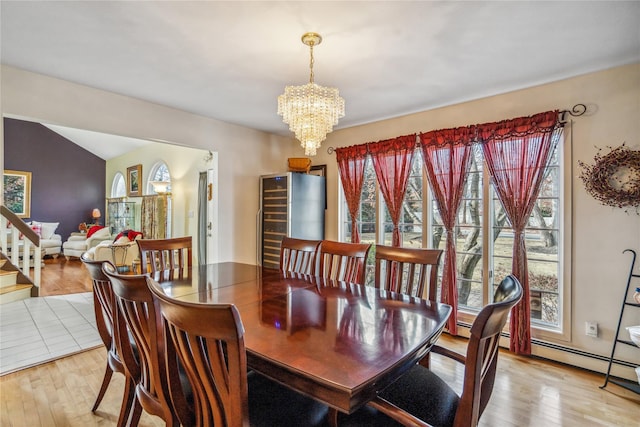 dining space with light wood-style flooring, stairs, a chandelier, and vaulted ceiling