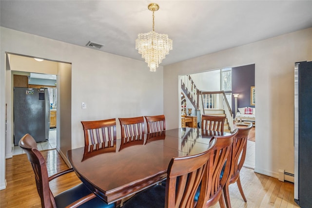 dining area featuring a chandelier, visible vents, light wood-style floors, stairs, and baseboard heating