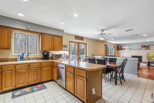 kitchen featuring dishwasher, open floor plan, a peninsula, light countertops, and a sink