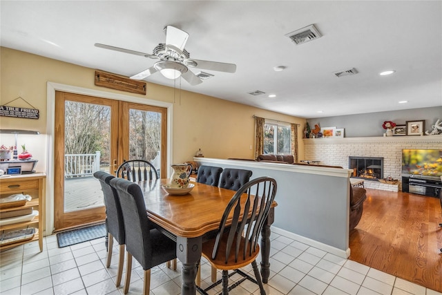 dining room featuring a brick fireplace, visible vents, and light tile patterned floors